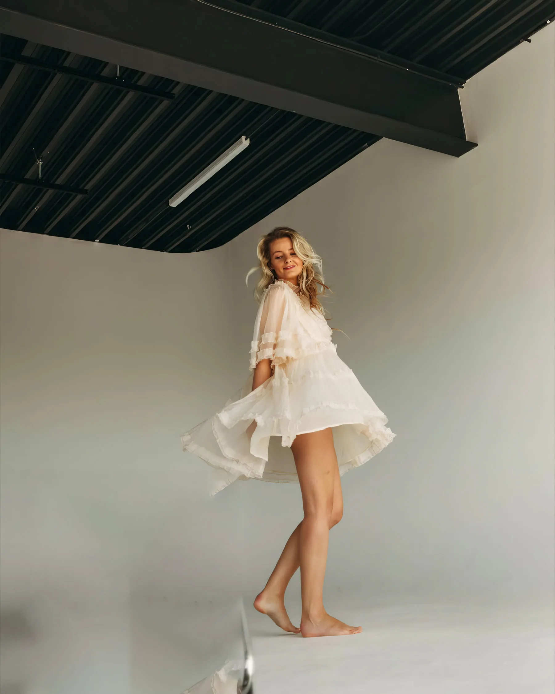 Veronika mid‑twirl in a sheer cream dress, hair caught in the studio fan