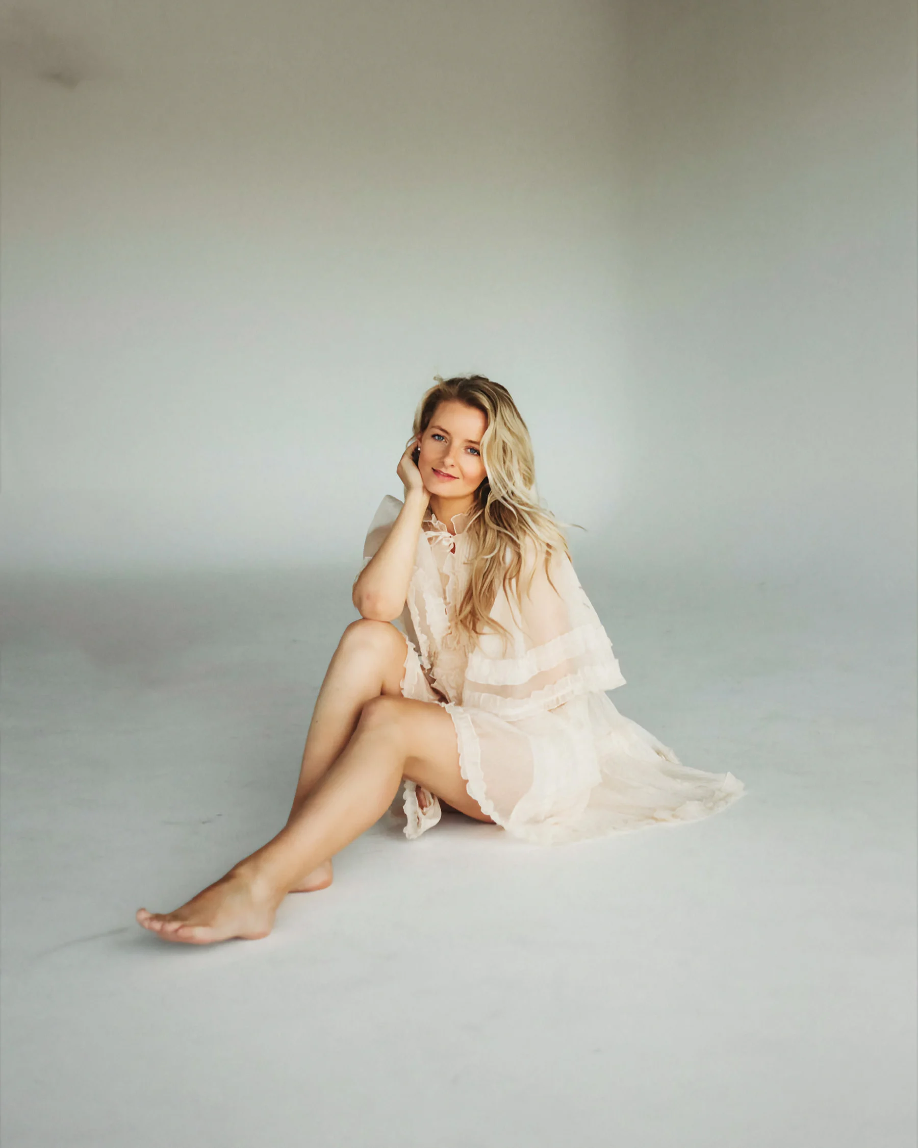 Veronika seated on a white studio floor in a sheer cream dress