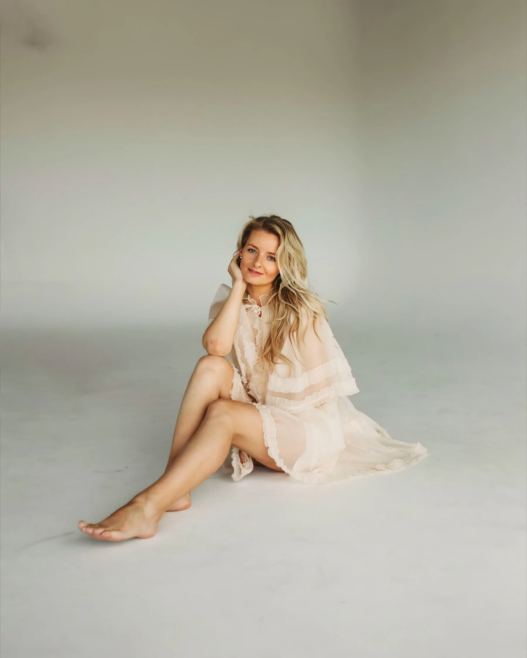 Veronika seated on a white studio floor in a sheer cream dress