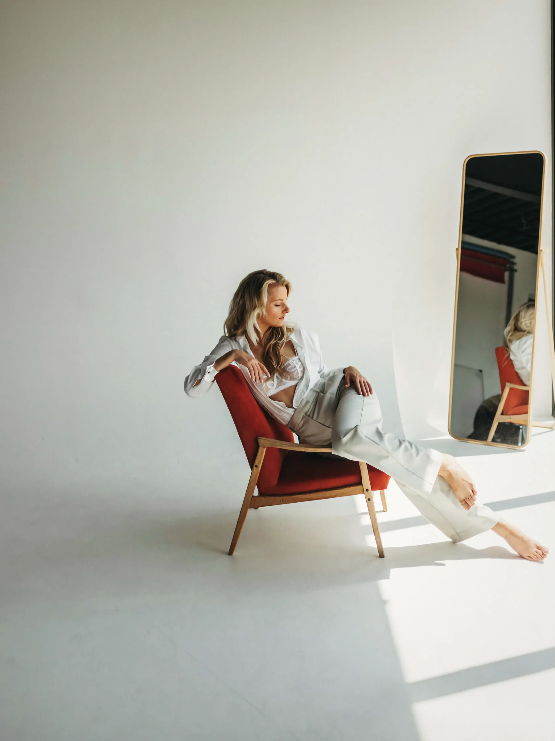 Veronika seated in a terracotta chair in a white studio, a mirror beside her