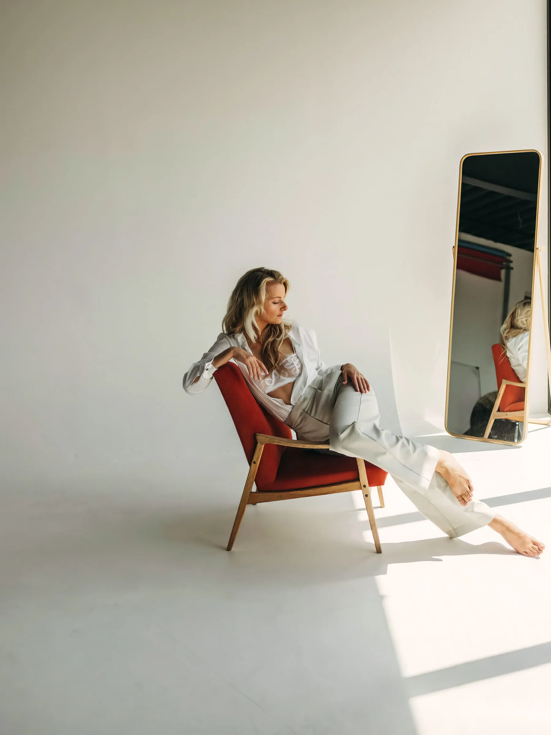 Veronika seated in a terracotta chair in a white studio, a mirror beside her